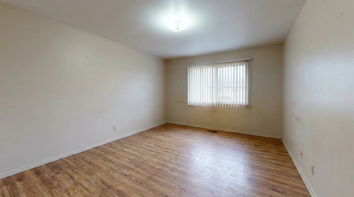 Leeres, unmöbliertes Wohnzimmer einer Ferienwohnung mit kahlen Wänden und Laminatboden